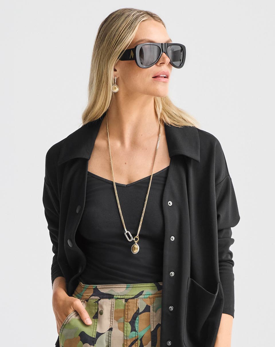 Model Wearing Elemental Topper in Black, V-Neck Cami in Black, Zip Line Skirt in Camo, Timepiece Earrings in Silver and Gold, Timepiece Necklace in Silver and Gold